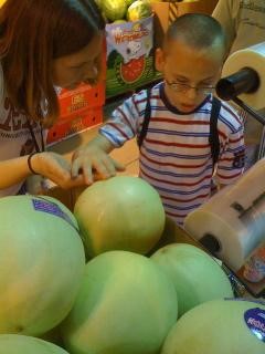 Boy at grocery store. An adult is helping him explore what melons feel like. She has her hand under his.
