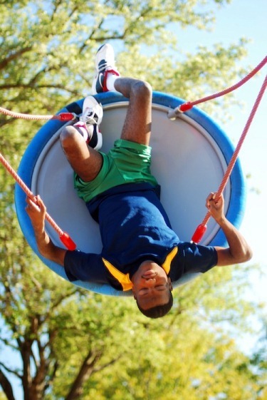 A boy swings upside down in a disc swing.
