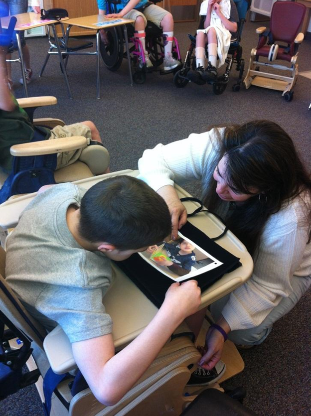 A boy and an adult during a lesson using a picture. The boy has his face very close to the picture.